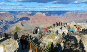 Many people standing along the Grand Canyon walk path with railings, enjoying panoramic views of the canyon cliffs and valleys.
