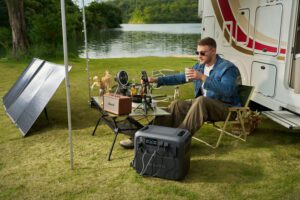 RV Tech & Safety Gear – 50 Smart Essentials for Road 3 Person sitting in a camping chair next to an RV with a solar-powered generator, solar panels, and a table with camping essentials.