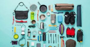 Essential camping gear laid out for a trip, including cookware, cups, utensils, and outdoor supplies.