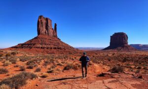Person standing in a desert landscape with two towering red rock formations in the background.