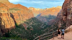 🌄 Lipan Point – Grand Canyon South Rim Overlook 4 Two people standing next to a railing at the top of a canyon, looking out over steep cliffs and expansive canyon scenery under a clear sky.