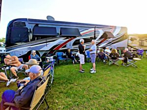 Large, brightly decorated RV trailer with multiple people sitting in chairs, enjoying a lively outdoor camping experience.