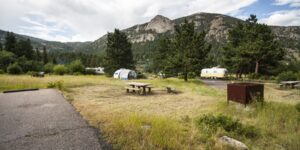 RV trailers and a tent with a picnic table in a wooded campground with mountain views