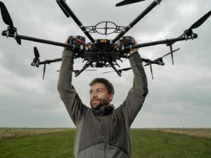Person holding a large black drone above their head outdoors.