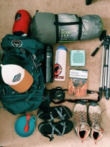 Top-down view of organized camping supplies on display, including backpacks, cooking gear, lanterns, and outdoor essentials neatly arranged on a wooden surface.