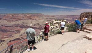 People standing behind a fence at the top of the Grand Canyon, admiring the scenic view.