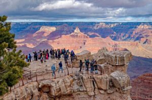 Many people standing along the Grand Canyon walk path with railings, enjoying panoramic views of the canyon cliffs and valleys.