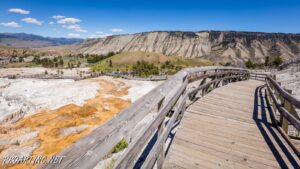 View of a Yellowstone geyser from a wooden walkway, with mountains in the background.