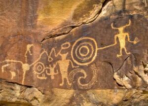 Large rock featuring intricate carvings and designs, set in a natural outdoor environment.