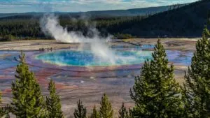 Grand Prismatic Spring in Yellowstone National Park with rising geothermal steam, colorful thermal waters, surrounding boardwalks, evergreen forests, and mountain scenery.
