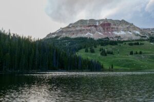 Yellowstone Lake – The Heart of Yellowstone National Park 3 Yellowstone Lake surrounded by evergreen forests, green mountain slopes, and rugged rocky peaks beneath a cloudy sky.