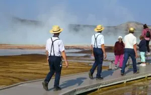 Visitors walking along a Yellowstone boardwalk beside steaming geothermal pools and colorful mineral deposits at Mammoth Hot Springs.