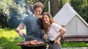 Two people cooking on a grill at a glamping campsite.
