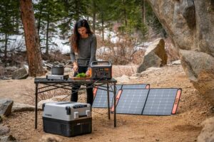 Woman preparing vegetables on a table outdoors, next to solar panels and a portable generator, enjoying eco-friendly camping.