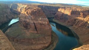 Panoramic view of Horseshoe Bend, showing the Colorado River curving through steep canyon walls, with RV parking area nearby.