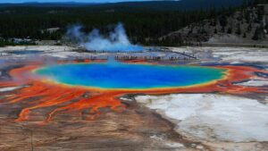 Grand Prismatic Spring in Yellowstone at sunset, displaying vivid rainbow colors with forest in the background.