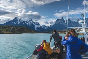 Several people on a boat enjoying a lake with mountains in the distance under a clear sky.