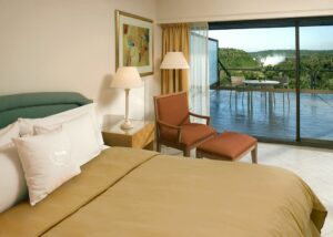 Gran Meliá Iguazú (Argentina) – Luxury With A Front-Row View of Iguazú Falls 🌊✨ 2 Hotel room with bed and chair, sliding glass door opening to rainforest view with Iguazú Falls visible in the distance.