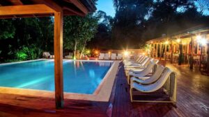 Outdoor pool with wooden deck, table and chairs, surrounded by forest.