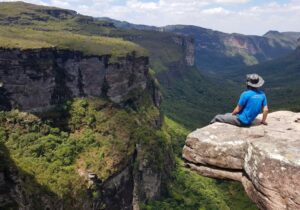 Person sitting on a ledge overlooking a steep canyon with dense South American rainforest below.