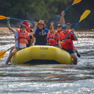 several people in a raft on a river wearing life jackets enjoying the day