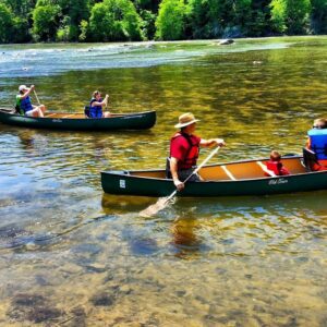 People canoeing in a river of clear water with trees in the background.