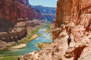 Person hiking in a steep canyon with a backpack, river flowing below, surrounded by vegetation