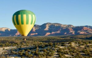 Yellow and green hot air balloon floating over a canyon plain with vegetation under a clear blue sky