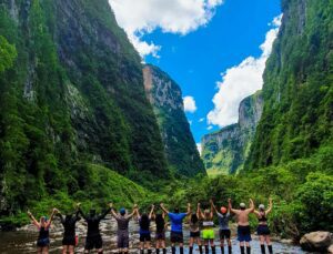 Several people hiking through Itaimbezinho Valley in Brazil, with tall canyon walls, dense rainforest vegetation, and a scenic trail under a clear sky.