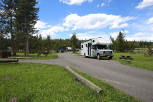 Modern RV parked at a scenic campground in Yellowstone National Park surrounded by pine trees, open campsites, and beautiful mountain landscapes.