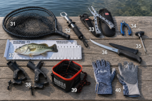 Fishing accessories neatly arranged on a wooden dock beside a calm lake, including a landing net, fish gripper, fishing pliers, line cutters, hook remover, fillet knife, fish measuring board, rod holders, portable bait bucket, and fishing gloves for freshwater and saltwater fishing.