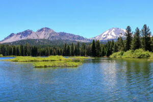 The Ultimate Yellowstone National Park Guide: Valleys, Lakes, Yellowstone River & waterfalls 3 Scenic mountain lake surrounded by evergreen forests and snow-capped peaks under a clear blue sky in Yellowstone National Park.