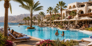 Luxury Red Sea resort with a large swimming pool, palm trees, lounge chairs, guests, and mountain and sea views in Egypt.