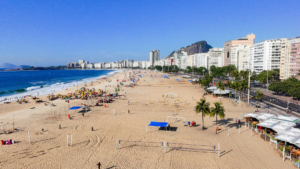 Rio’s Beaches, Coastal Trails & Outdoor Adventures 4 Wide view of Copacabana Beach in Rio de Janeiro with beach volleyball courts, visitors, palm trees, blue ocean, and beachfront buildings.