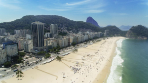 Rio’s Beaches, Coastal Trails & Outdoor Adventures 19 Aerial view of Rio de Janeiro’s beachfront with hotels and city buildings lining the sandy beach, surrounded by mountains and the Atlantic Ocean.