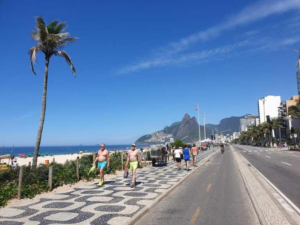 Rio’s Beaches, Coastal Trails & Outdoor Adventures 5 People walking along Rio de Janeiro’s beachfront promenade beside the beach, bike lane, palm trees, and mountains between Copacabana and Ipanema.