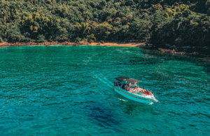 🏝️ Ilha Grande – Beaches, Rainforest Trails, Kayaking & Island Adventures 11 Boat tour cruising through turquoise water beside a lush rainforest coastline on Ilha Grande, Brazil.