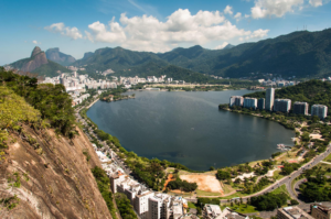 Rio’s Beaches, Coastal Trails & Outdoor Adventures 15 Panoramic view of Rodrigo de Freitas Lagoon surrounded by Rio de Janeiro neighborhoods, green mountains, roads, and tropical scenery.