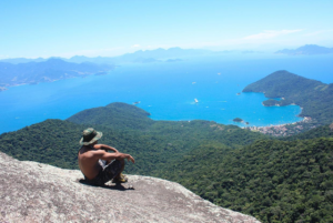 🏝️ Ilha Grande – Beaches, Rainforest Trails, Kayaking & Island Adventures 8 Hiker overlooking Ilha Grande’s rainforest-covered mountains, coastline, and blue ocean from a high mountain viewpoint in Brazil.