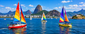 Colorful sailboats sailing across Guanabara Bay in Rio de Janeiro with Sugarloaf Mountain, coastal mountains and the city skyline in the background.
