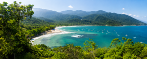 🏝️ Ilha Grande – Beaches, Rainforest Trails, Kayaking & Island Adventures 1 Panoramic view of Ilha Grande, Brazil, featuring turquoise ocean water, a tropical beach, lush rainforest-covered mountains, and boats along the coastline.