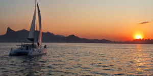 Sailboat cruising across the water at sunset with Rio de Janeiro’s mountains and coastline in the background.