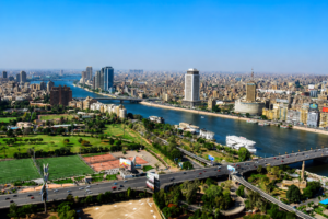Aerial view of the Nile River flowing through Cairo, Egypt, surrounded by city buildings, bridges, roads, parks, and waterfront development.