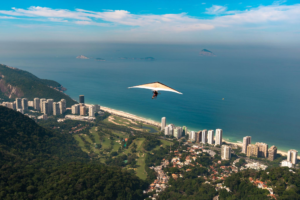 Rio’s Beaches, Coastal Trails & Outdoor Adventures 9 Hang glider soaring above Rio de Janeiro’s coastline with São Conrado Beach, Atlantic Ocean, forested mountains, and city buildings below.
