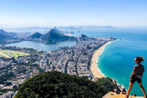 Rio’s Beaches, Coastal Trails & Outdoor Adventures 8 Hiker overlooking Ipanema and Leblon from a high viewpoint near Morro Dois Irmãos in Rio de Janeiro, with beaches, city buildings, lagoon, mountains, and Atlantic Ocean below.