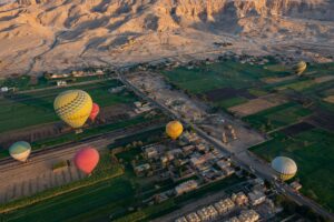 Hot air balloons flying over the green Nile Valley farmland and desert mountains near Luxor, Egypt, during the early morning.