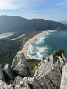 Elevated trail view overlooking Praia do Perigoso with a long sandy beach, Atlantic waves, forest-covered mountains and rugged rocks along Rio de Janeiro’s wild coastline.