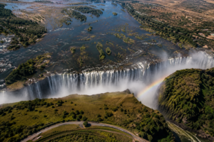 Aerial view of Victoria Falls and the Zambezi River showing the massive waterfall, river islands, rising mist, deep gorge and rainbow.