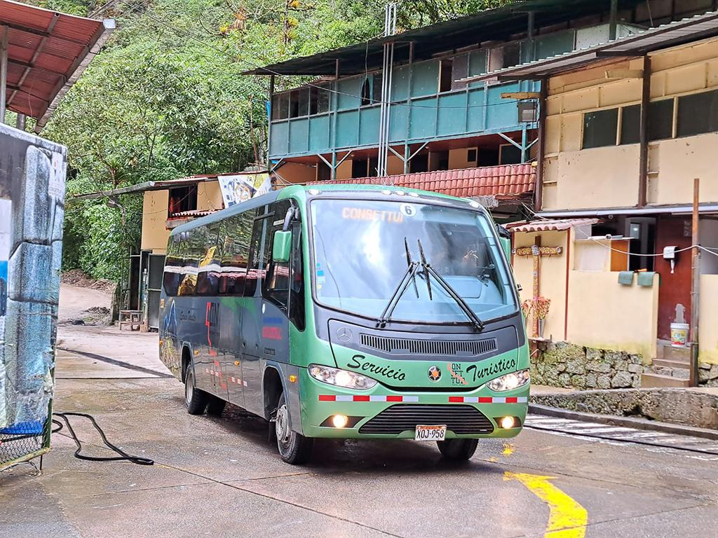 Green Consettur tourist shuttle bus on a street in Aguas Calientes, Peru, illustrating transportation to the Machu Picchu archaeological site.