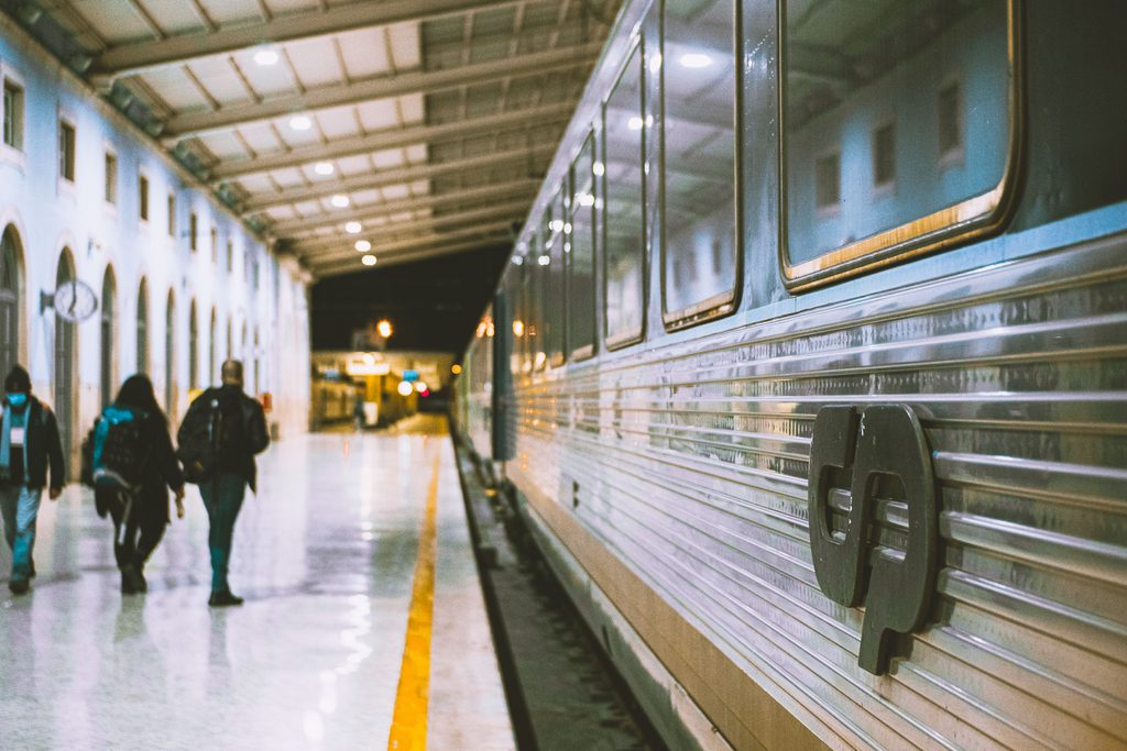 Travelers with backpacks walking along a covered railway platform beside a passenger train before departure.